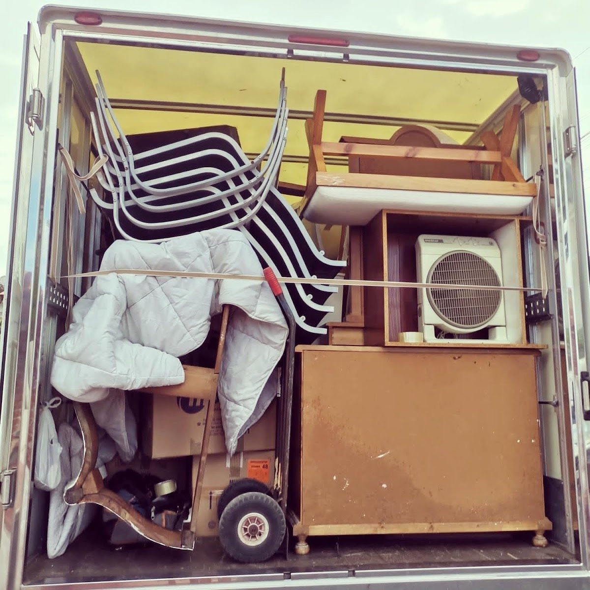 A trailer filled with stacked furniture, including chairs, a dresser, and an air conditioner.