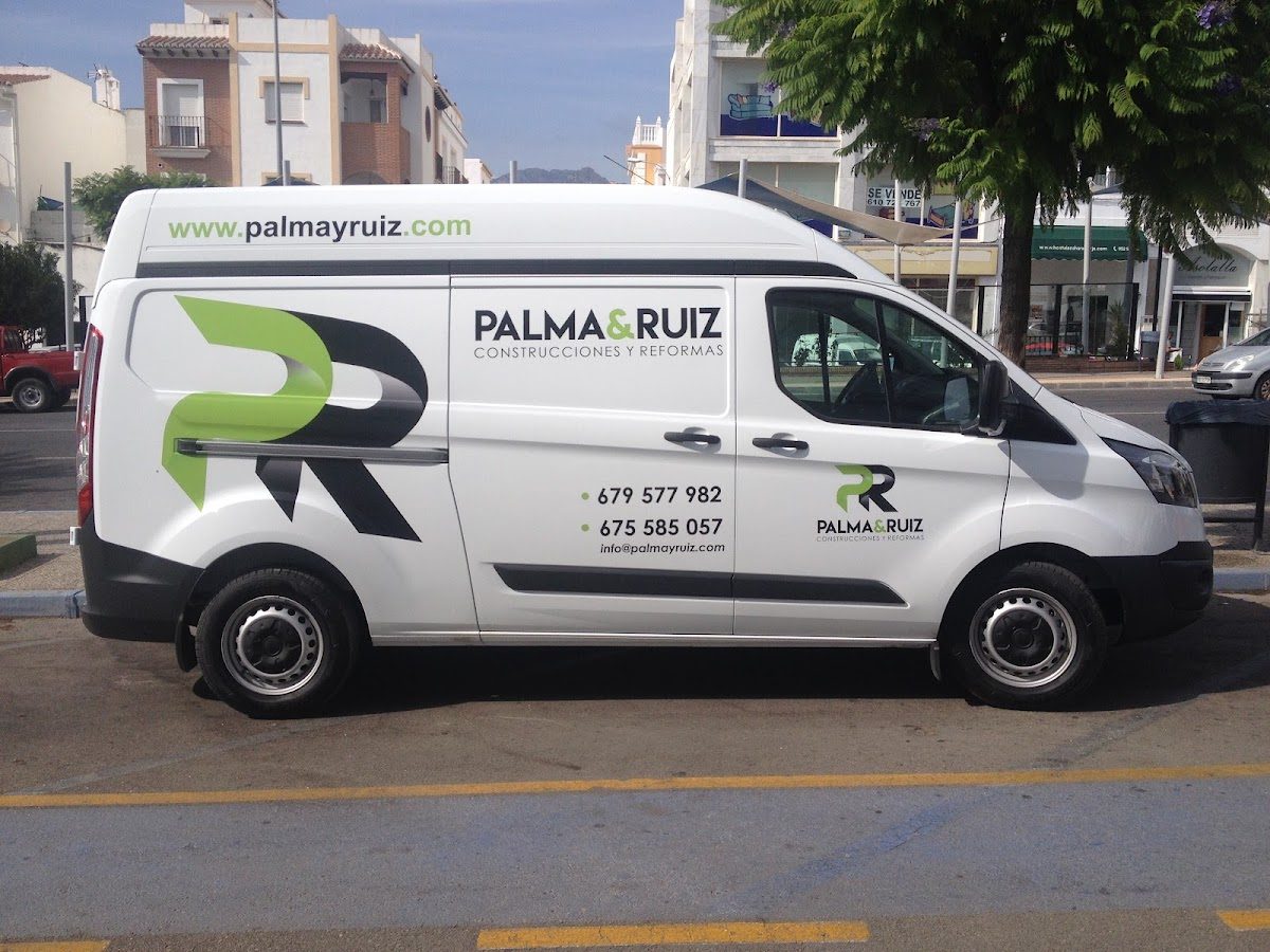 A white van with the logo "PALMA & RUIZ" parked on the street near trees and buildings.