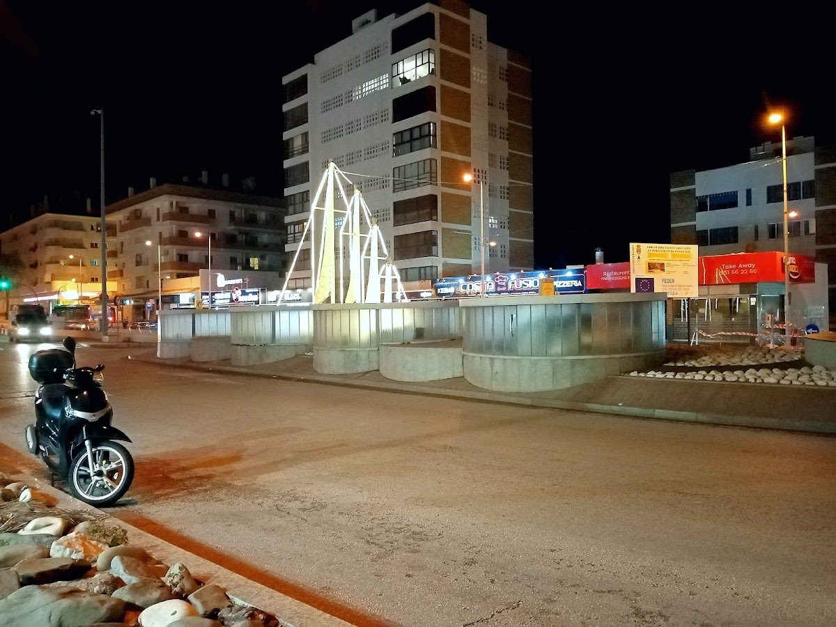 The illuminated PSEUDO SHIP attraction features a modern design in Benalmádena, surrounded by buildings and signage.