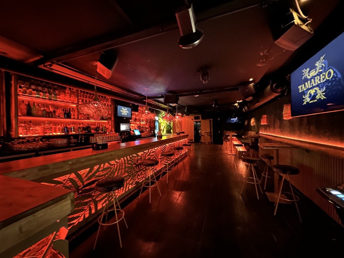 The interior of Pub Tamareo features a stylish bar with vibrant red lighting and modern seating.