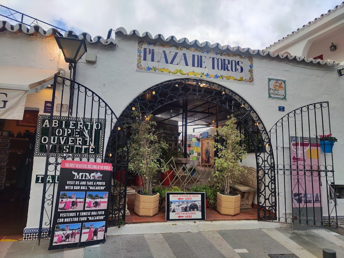 La entrada a la Plaza de Toros en Mijas Pueblo, con señalización decorativa y asientos al aire libre.