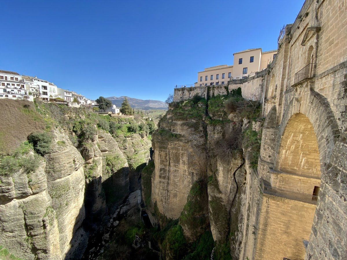 Vista del puente Nuevo de Ronda, que atraviesa un profundo desfiladero, con acantilados y edificios circundantes bajo un cielo azul despejado.