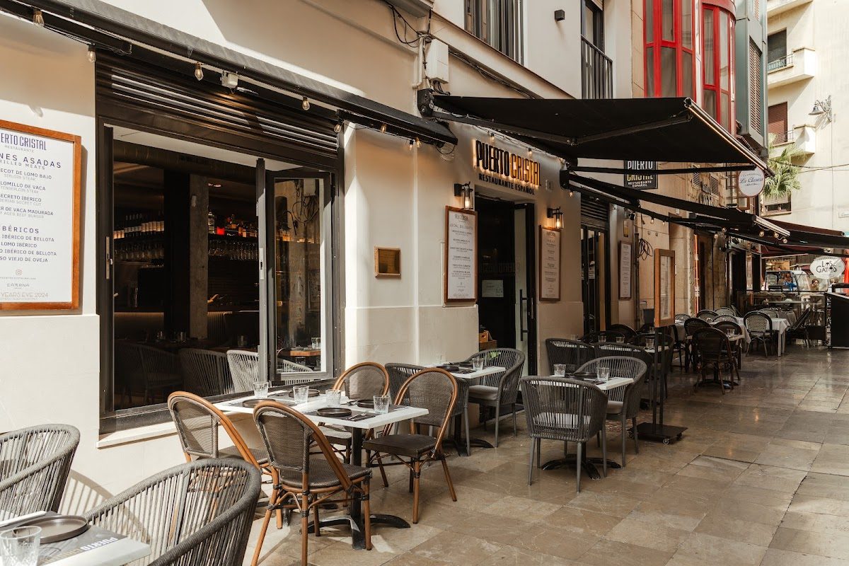 El restaurante Puerto Cristal cuenta con una terraza al aire libre con sillas de mimbre y una fachada acogedora en una calle con encanto.