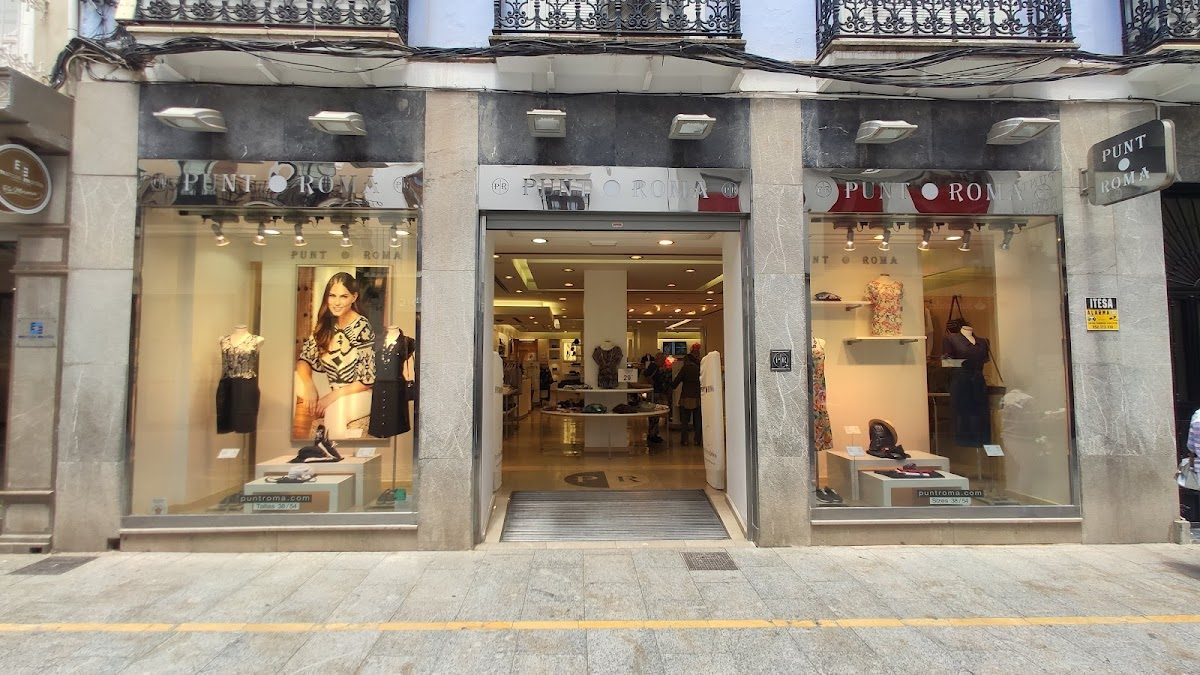 La fachada de PUNT ROMA cuenta con grandes ventanales de cristal que exhiben ropa y accesorios elegantes.
