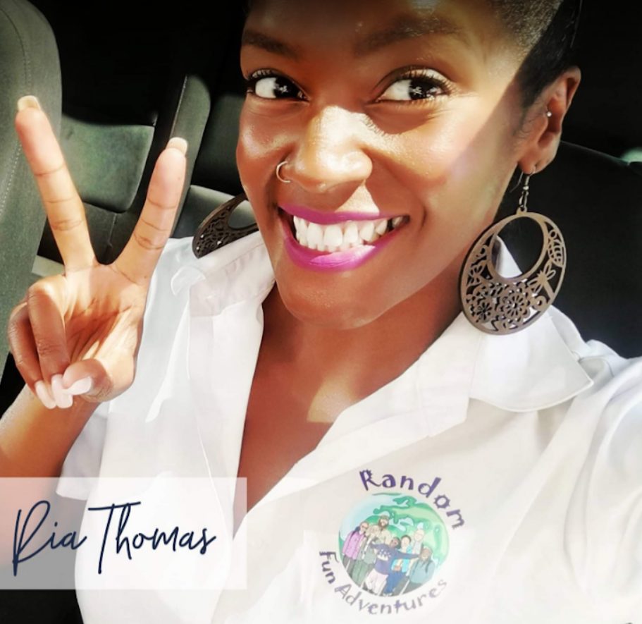 A smiling woman wearing a "Random Fun Adventures" shirt and large earrings, giving a peace sign.