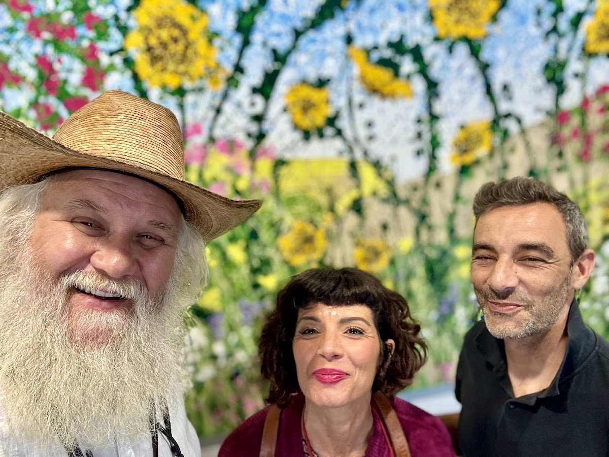 Un trío sonriente posa frente a un vibrante mural floral en Raven Art Studio Marbella.