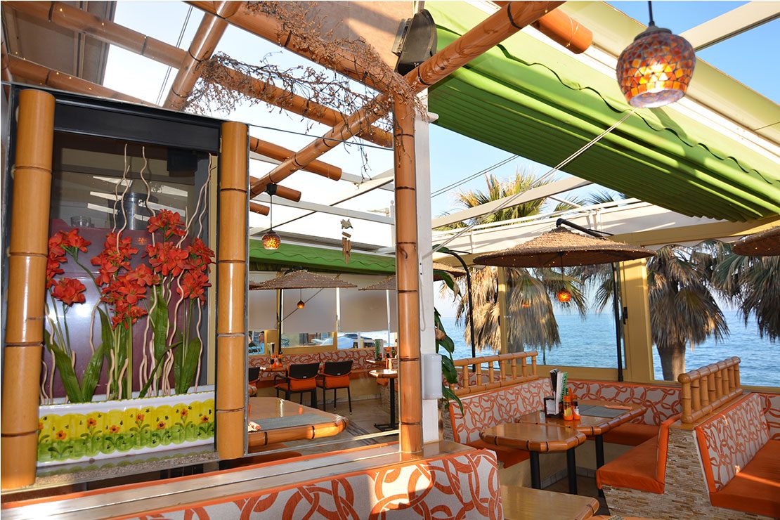 The interior of Restaurant Bamboo features bamboo decor, vibrant floral art, and a view of the sea.