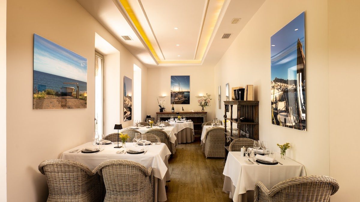 Elegante comedor en el Restaurante Candela Marbella, con sillas de mimbre y grandes fotografías de la costa en las paredes.