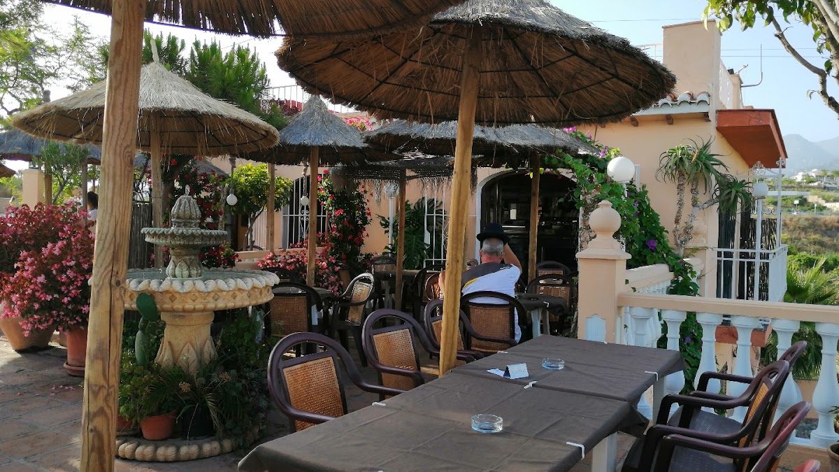 Restaurante El PUENTE features a charming outdoor seating area with thatched umbrellas and vibrant flowers.