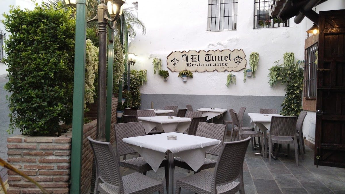 Outdoor seating area with tables and chairs at Restaurante El Tunel, surrounded by greenery.