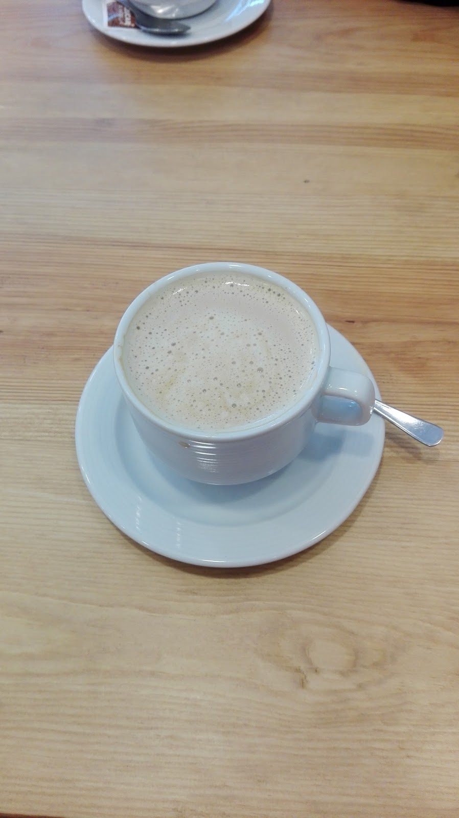 Una taza de café azul claro sobre un platillo blanco, colocada sobre una mesa de madera.