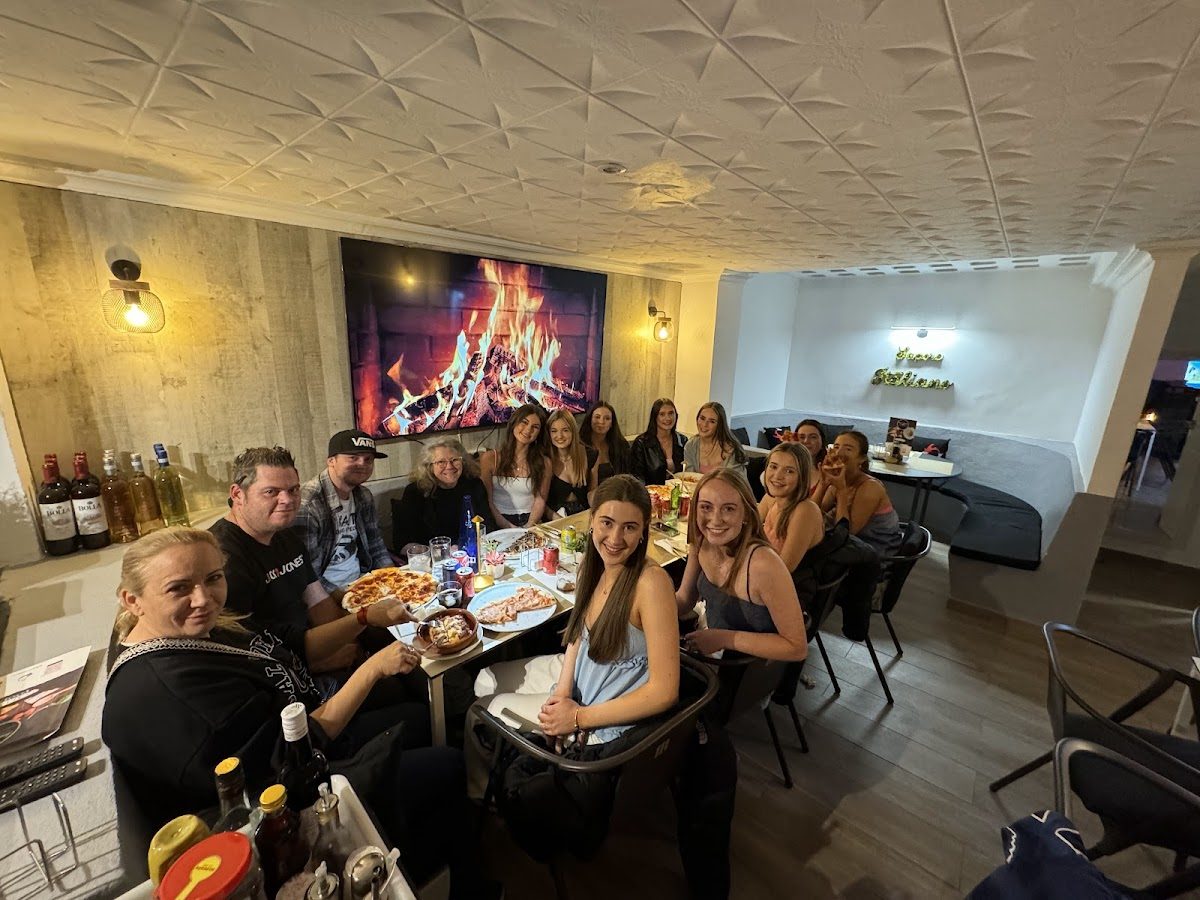 A group of diners enjoying a meal around a table in Sapore Italiano, with a fireplace in the background.