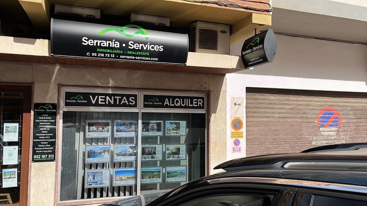 Fachada de la tienda de Serrania Services con letreros y anuncios inmobiliarios exhibidos en el escaparate.