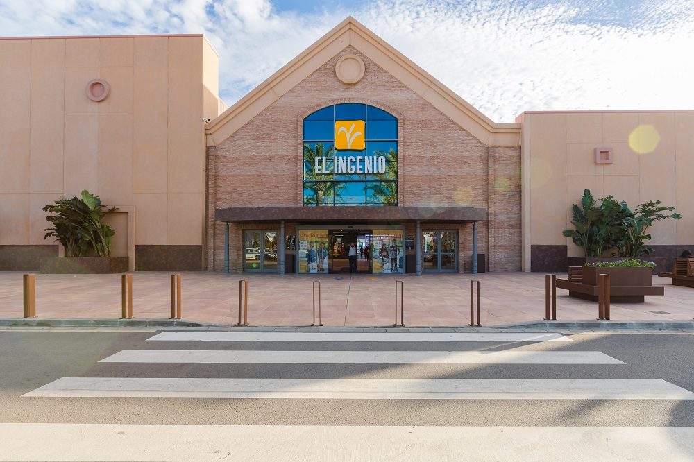 The exterior of Shopping Centre El Ingenio features a large entrance with a prominent sign and landscaped surroundings.