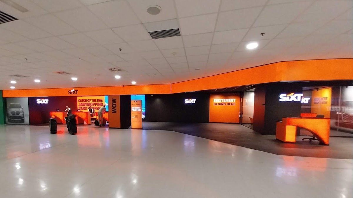 SIXT Alquiler de Coches cuenta con un mostrador de alquiler de coches moderno con detalles en color naranja brillante en el aeropuerto de Málaga.