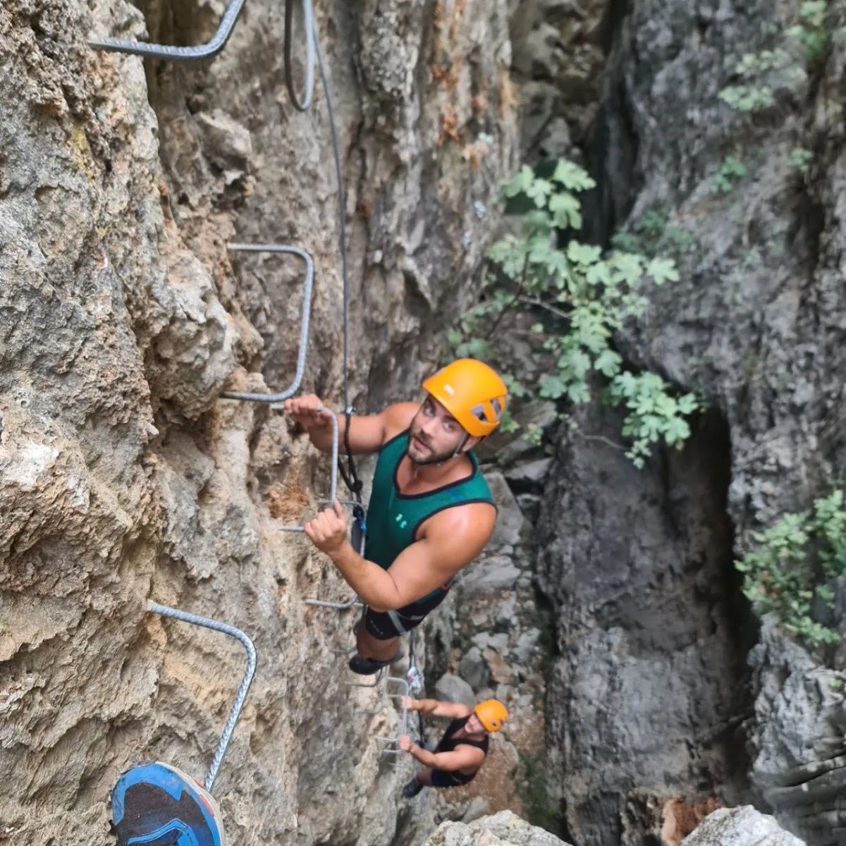 Two climbers ascend a rocky cliff using metal rungs, wearing helmets and harnesses, at South Coast Aventuras.