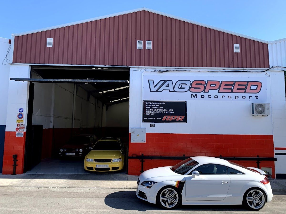 Vista exterior de ST Racing Autos con un coche blanco aparcado delante y dos coches visibles dentro del garaje.