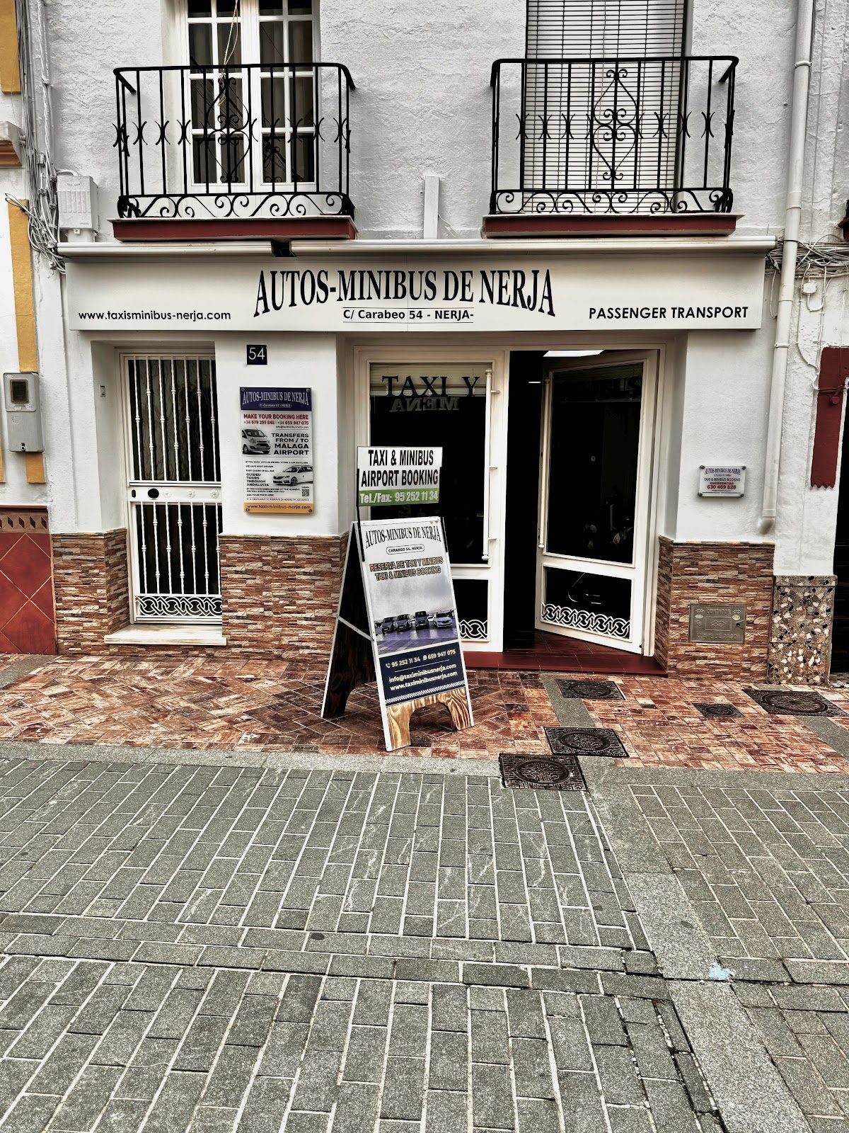 Vista exterior de un minibús taxi en Nerja, donde se aprecian la entrada y la señalización para el servicio de transporte de pasajeros.