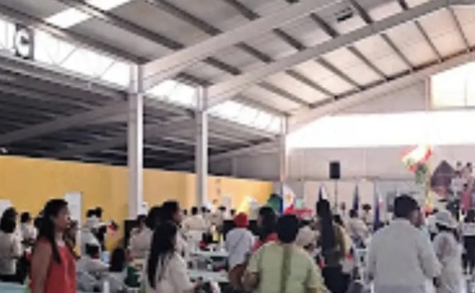 A spacious indoor event venue filled with attendees and colorful flags at TeVienes Eventos Carpa San Pedro Alcántara.