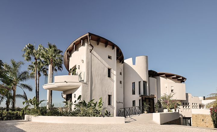 The Sanctuary Marbella features a modern architectural design with palm trees and a spacious entrance.