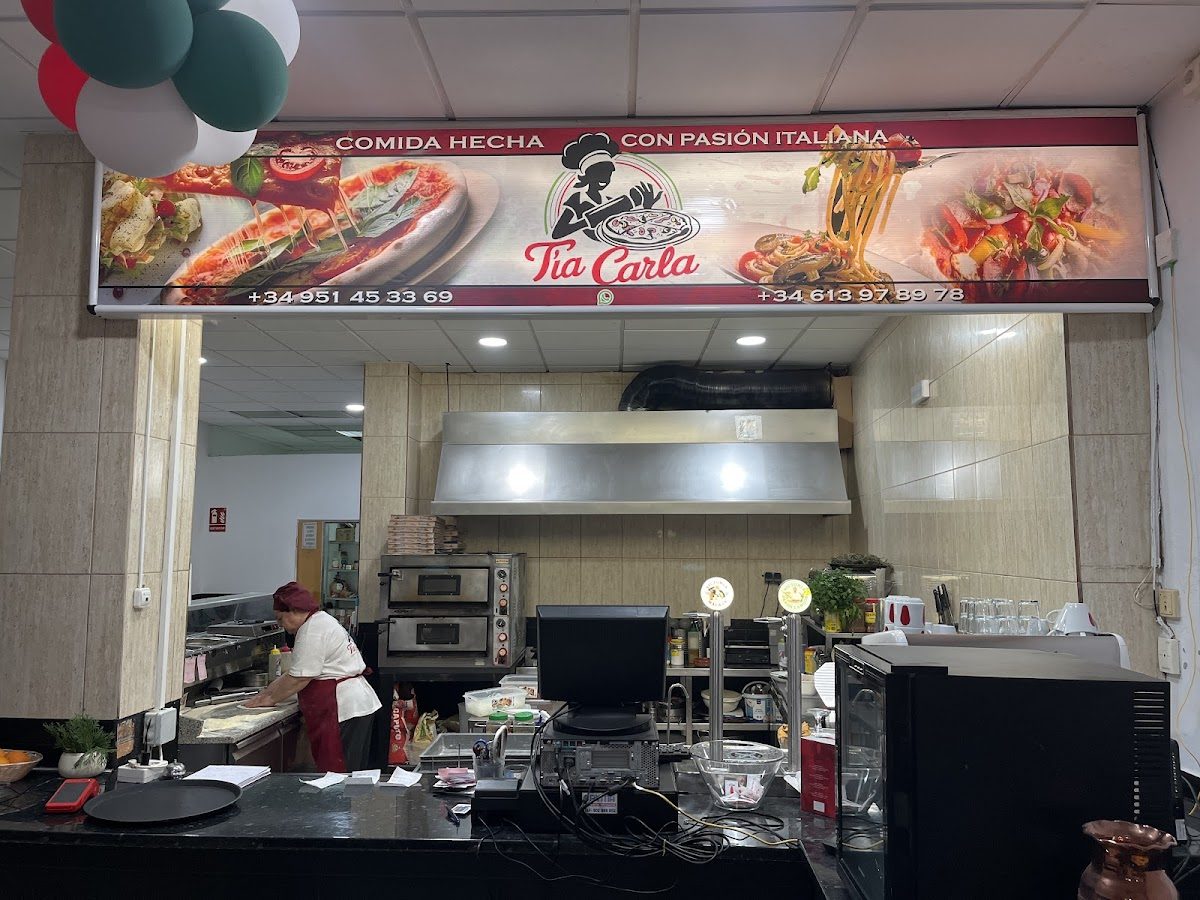 Interior view of Tía Carla restaurant showing kitchen area, staff preparing food, and colorful signage.