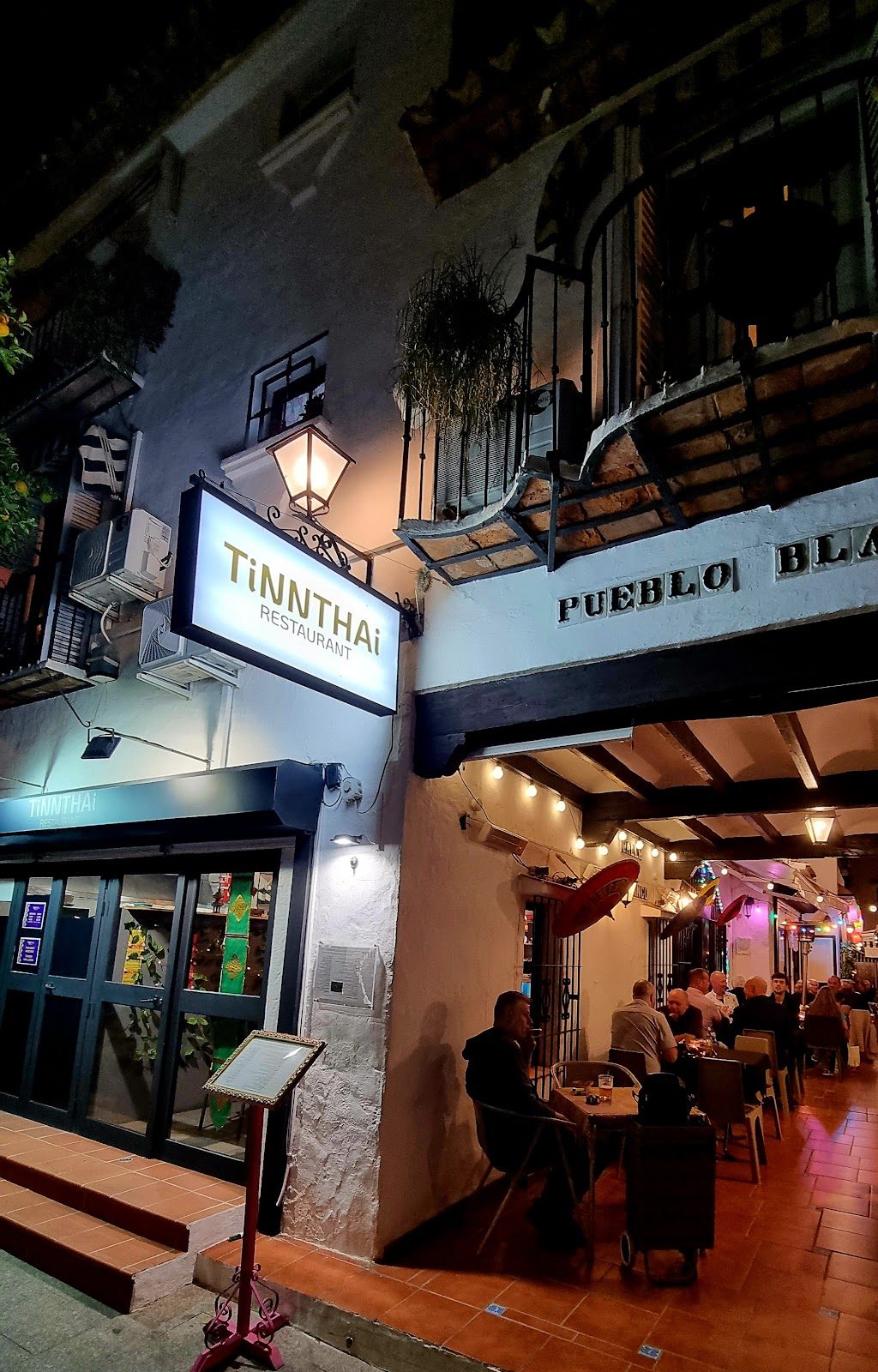 Vista exterior del restaurante tailandés TiNNTHAi en Torremolinos, con terraza y letreros iluminados.