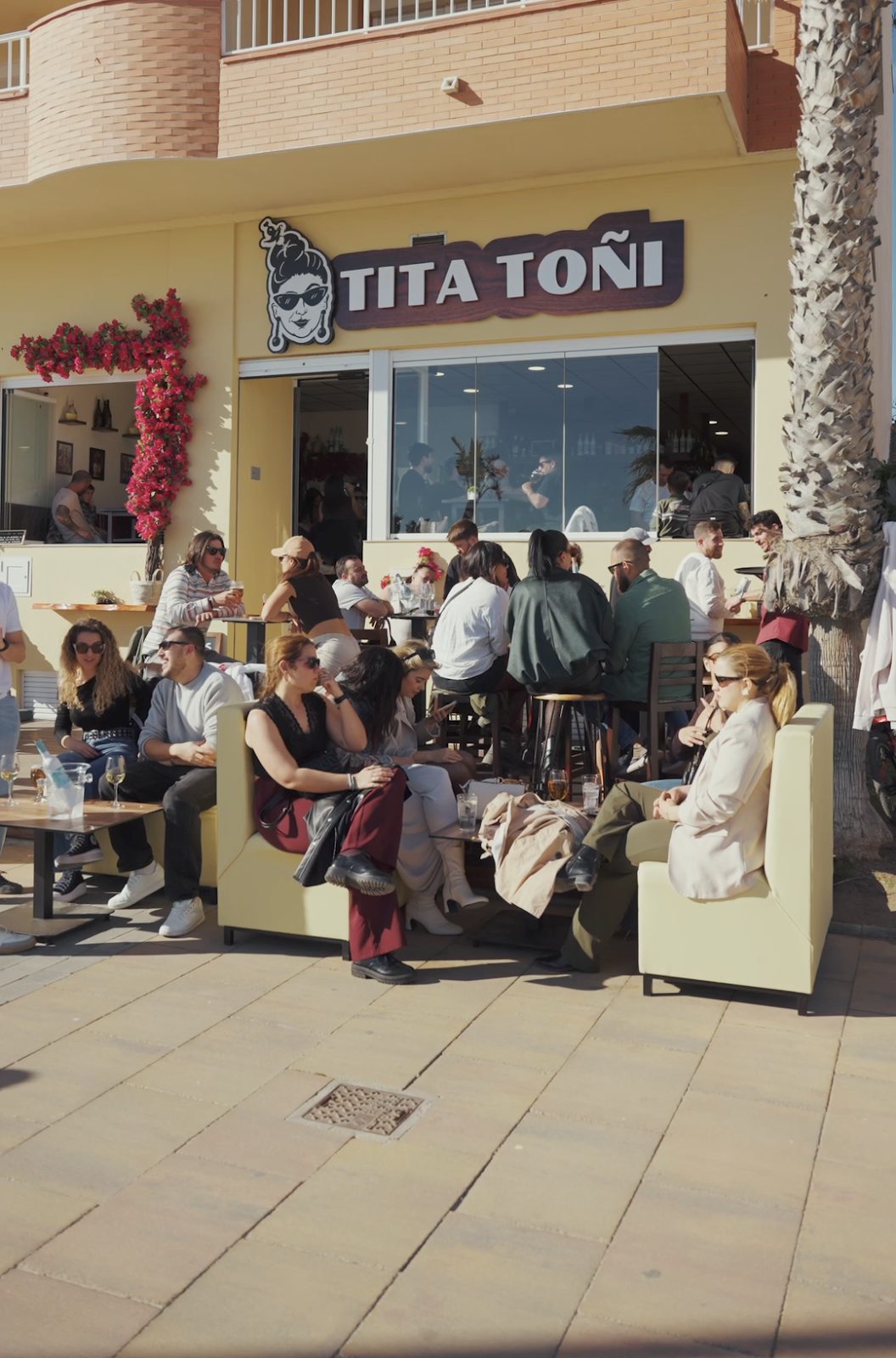 Outdoor seating area at TITA TOÑI with patrons enjoying drinks and a lively atmosphere.