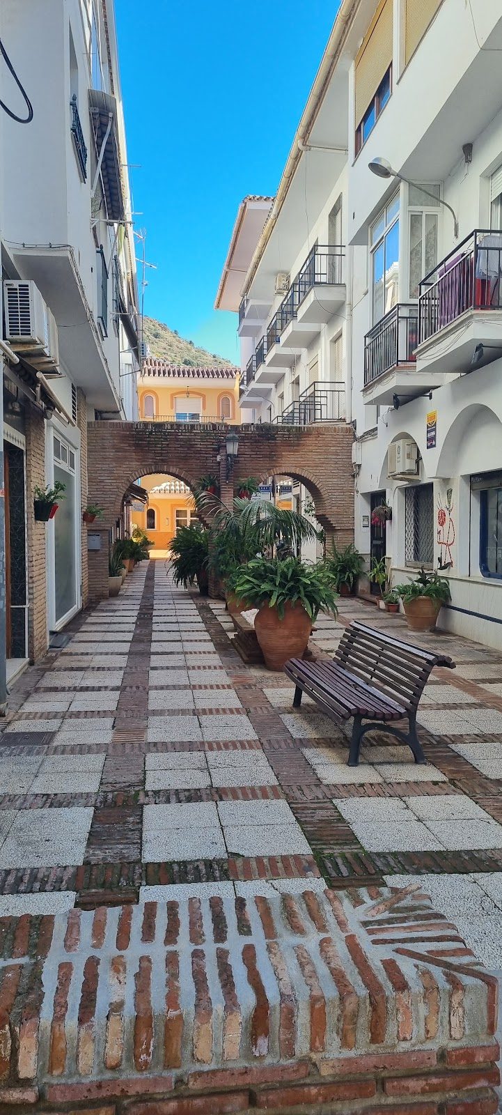 A charming pedestrian pathway with potted plants and benches in Torrox, Málaga.