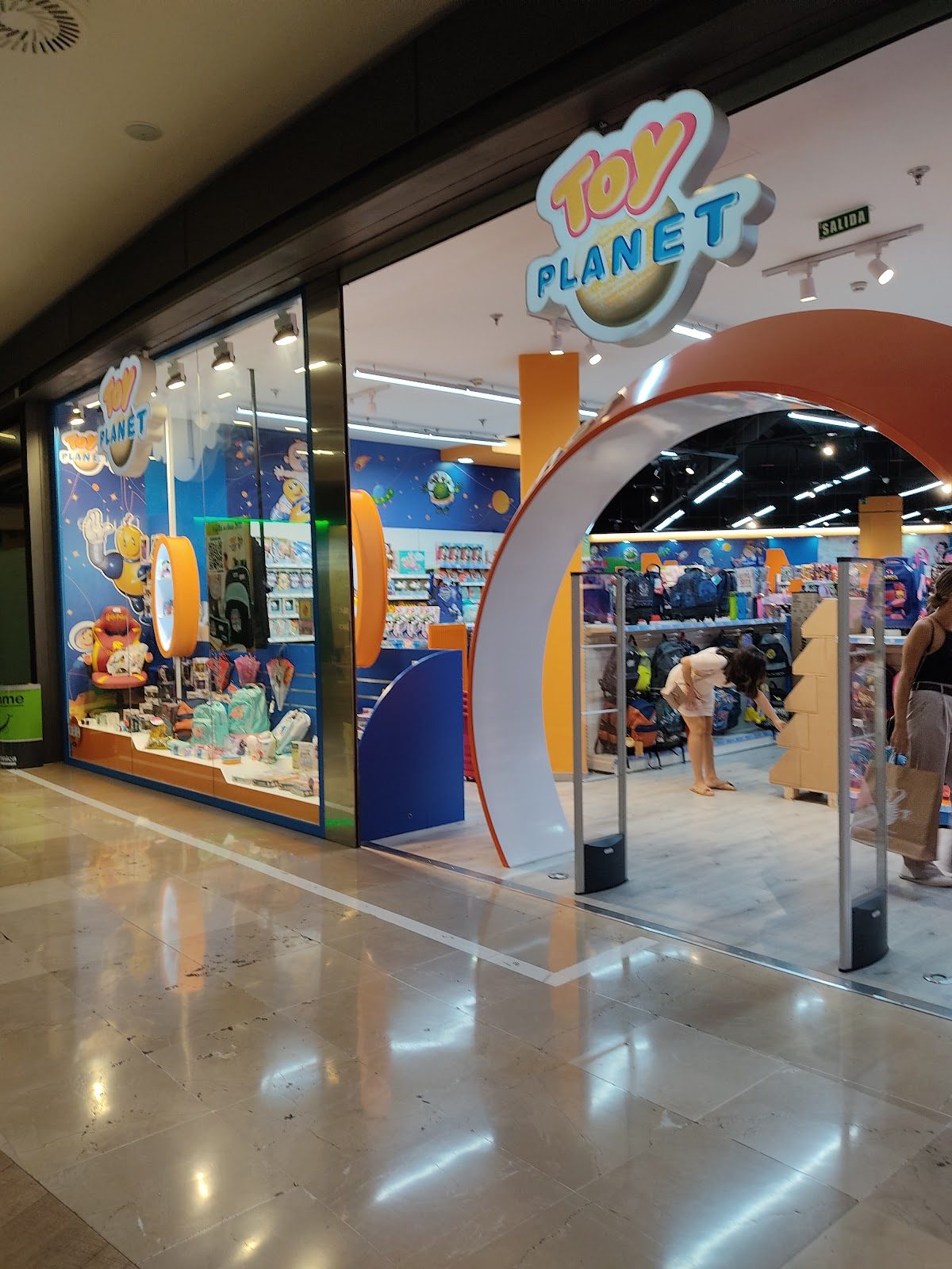 Brightly colored storefront of Toy Planet Antequera with toys displayed inside and shoppers browsing.