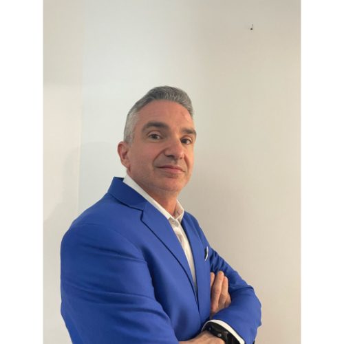 Un profesional con traje azul posa con seguridad sobre un fondo claro.