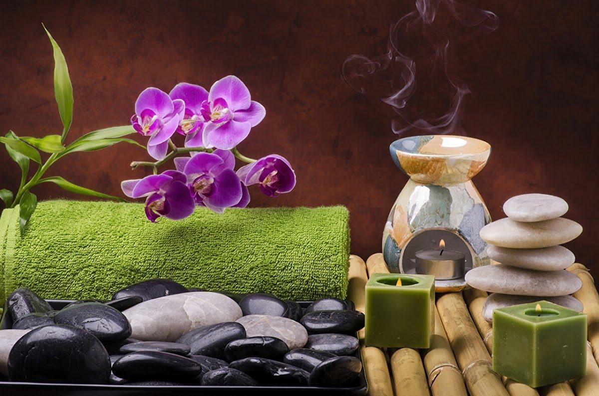 Un arreglo sereno con piedras, velas, un quemador de aceites y orquídeas moradas, que evoca un ambiente de spa.