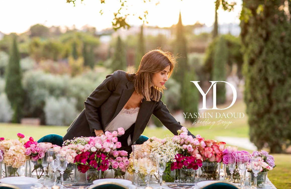 A wedding planner arranges a beautifully set table adorned with colorful flowers in an outdoor setting.