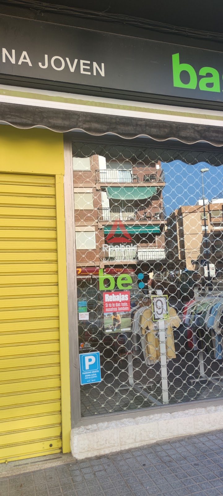 The storefront of Zona Joven features a closed metal gate and a sign with promotional offers visible in the window.